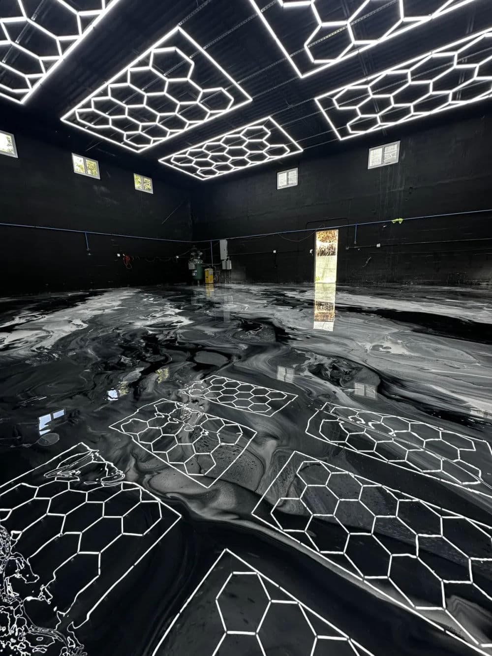 Stylish black room with hexagonal patterns on a glossy floor and illuminated ceiling design.
