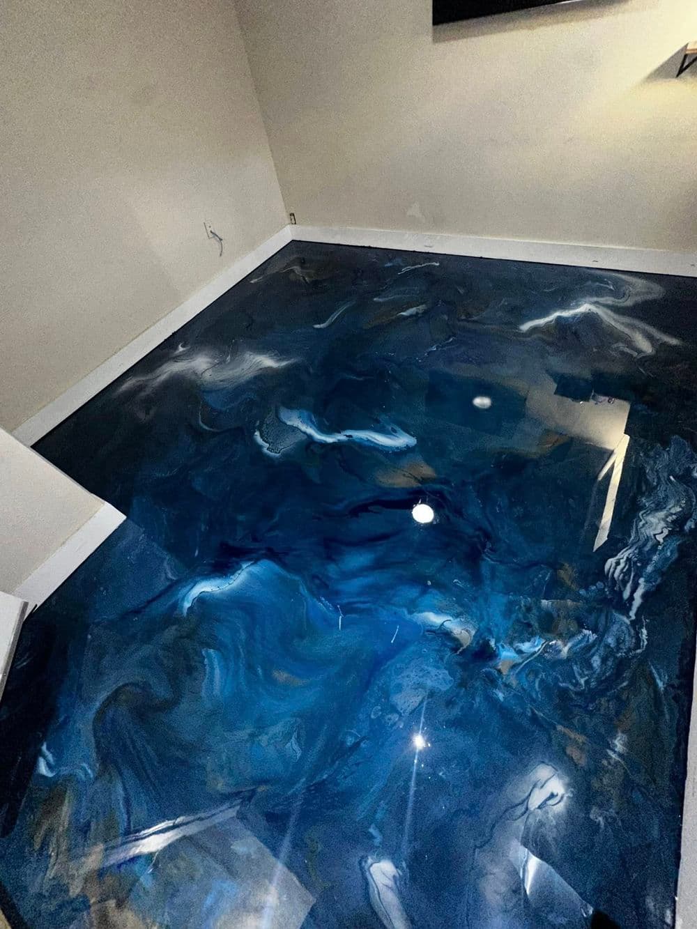 Glossy blue epoxy resin floor with fluid patterns in a modern room setting.
