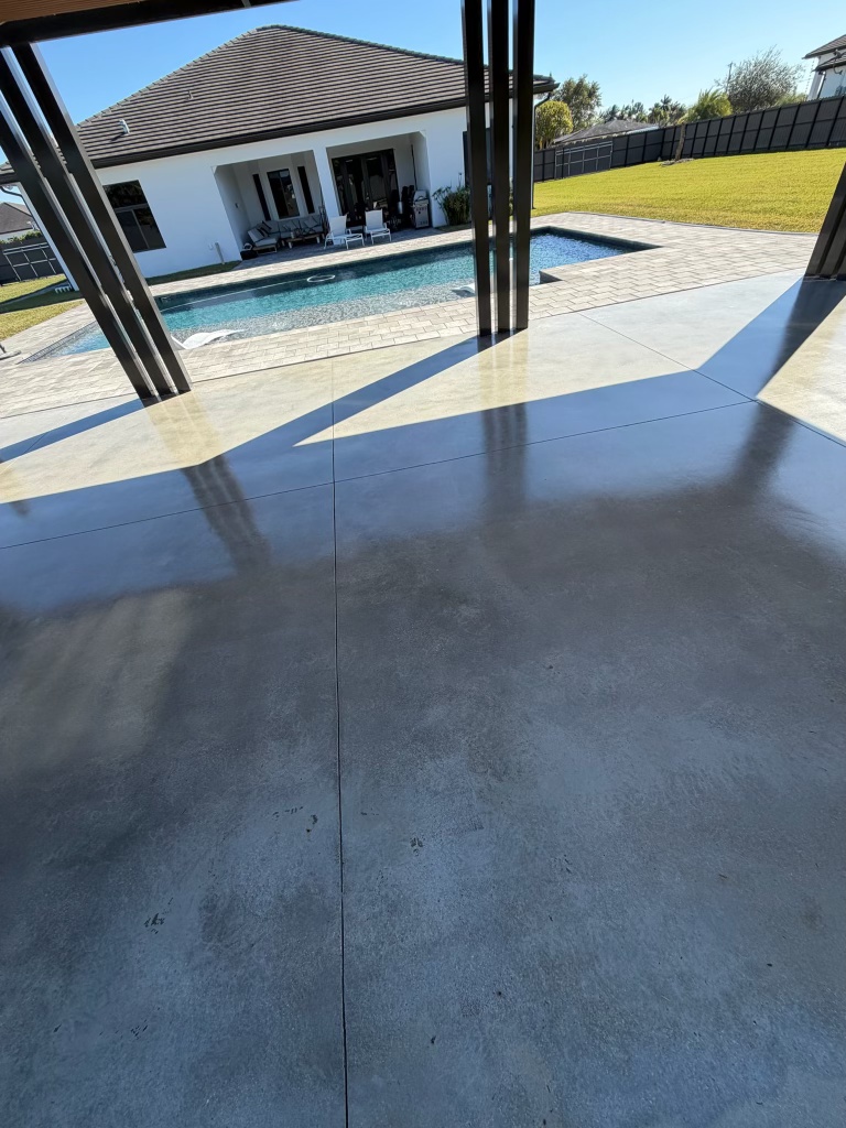 Polished gray concrete pool deck under a screened lanai, pool and paver coping behind it
