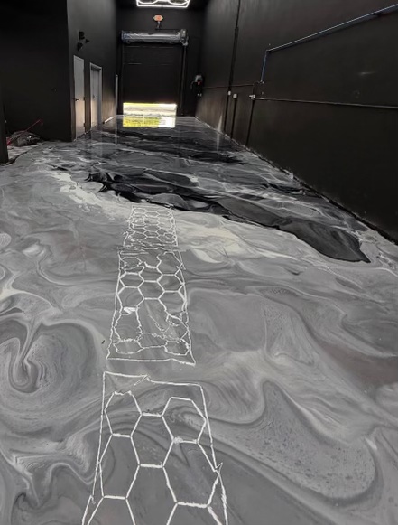 Gray and white metallic epoxy walkway with a white hexagon line inlay running down a dark-walled commercial corridor toward a lit doorway